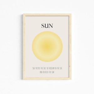 May include: A framed print with a yellow sun illustration and the text "SUN" in black. The quote "'SHE TASTED THE SALT OF FREEDOM IN THE SEA, AND REVELED THE SUN'" is printed below the sun.