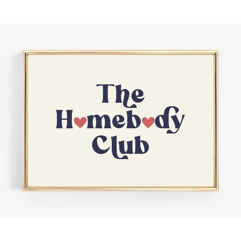 May include: A framed print with a cream background and gold frame. The text "The Homebody Club" is in navy blue with two red hearts.