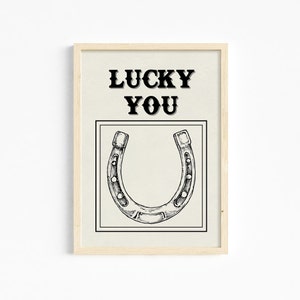 May include: A framed print with a black and white illustration of a horseshoe and the text "LUCKY YOU" in black.