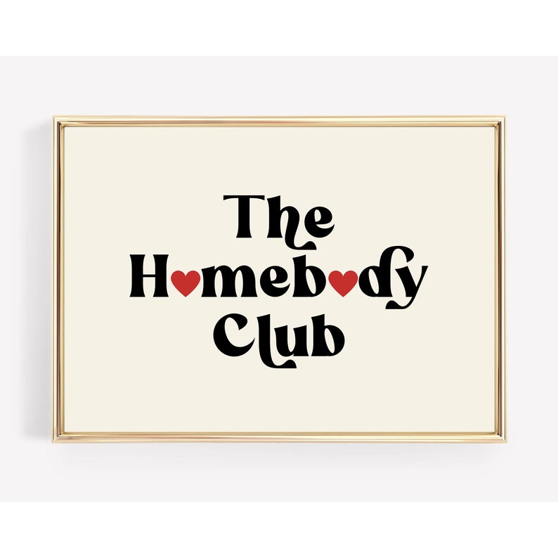 May include: A gold framed print with a white background and black text that reads "The Homebody Club" with two red hearts.