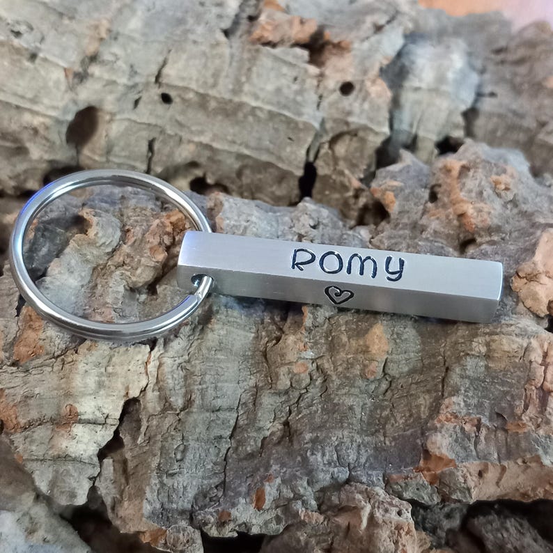 Op de afbeelding: Zilveren sleutelhanger met een staafvormige hanger gegraveerd met de naam "Romy" en een klein hartje.
