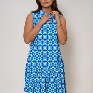 May include: Sleeveless dress with a geometric pattern in shades of blue, white, and green. The dress features a collared neckline with a white zipper and a ruffled hem. The dress is knee-length.