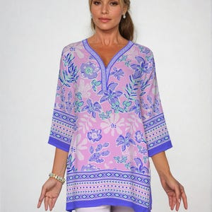 May include: A pink and purple floral print tunic top with a V-neck and 3/4 sleeves. The top has a blue and white geometric border around the bottom.
