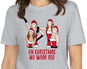 以下が含まれることがあります： サンタの衣装を着た4人の女性が描かれたグレーのTシャツ。グラフィックの下に「On Christmas We Wear Red」というテキストが印刷されています。