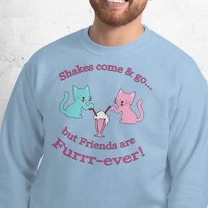 Può includere: Una felpa blu chiaro con una grafica di due gatti dei cartoni animati che condividono un milkshake. Il testo sulla felpa recita "Shakes come & go... but Friends are Furrr-ever!"