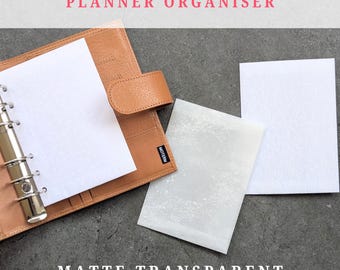 May include: A tan leather planner with a silver binder, open to show white paper. The image also shows matte transparent sheets and the text "PLANNER ORGANISER" and "MATTE TRANSPARENT".
