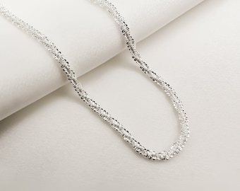 May include: A silver chain necklace with a delicate, twisted design. The chain is made of small, linked circles.