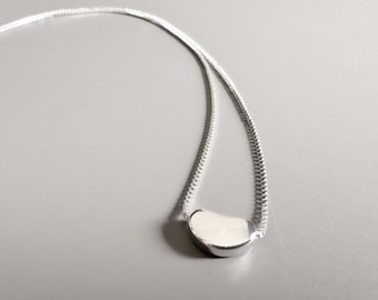 May include: A silver chain necklace with a small, smooth, crescent-shaped pendant.
