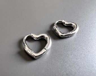 May include: A pair of silver heart-shaped hoop earrings. The earrings are made of metal and have a smooth finish.