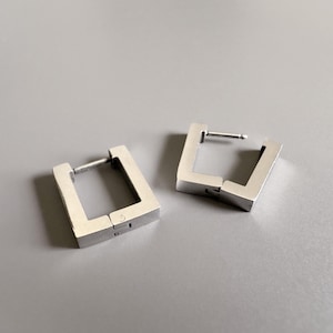 Könnte beinhalten: Ein Paar silberne quadratische Creolen. Die Ohrringe sind aus Metall und haben ein schlichtes, modernes Design.
