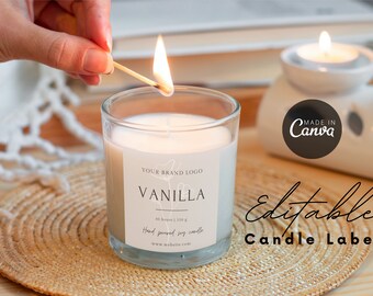 May include: A lit vanilla-scented candle in a clear glass jar, with a label that reads "Vanilla" and "Hand poured soy candle." The candle is on a woven mat. The text "Editable Candle Label" is also visible.