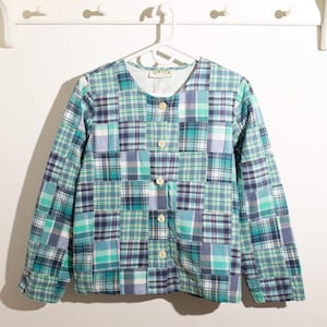 May include: A long-sleeved patchwork jacket in shades of blue, green, and white, with a button-up front. The jacket features a plaid pattern and the brand name "ORVIS" is visible on the collar.