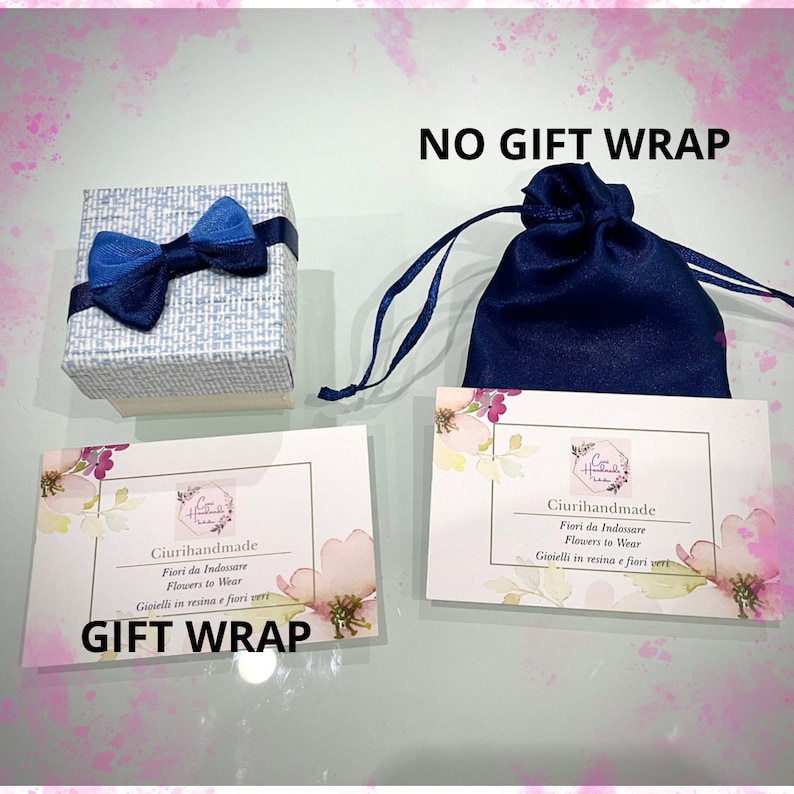 May include: Two gift wrapping options for a small item. The first option is a blue gift bag with a drawstring closure. The second option is a small white box with a blue bow. Both options have a card with the text "Ciurihandmade" and "Fiori da Indossare" in Italian and "Flowers to Wear" in English. The card also says "Gioielli in resina e fiori veri" in Italian and "Jewelry in resin and real flowers" in English. The text "NO GIFT WRAP" is written in black on a white background above the blue gift bag. The text "GIFT WRAP" is written in black on a white background below the white box.