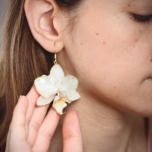 May include: White orchid flower earrings with gold-tone hooks. The earrings are made with real pressed flowers.