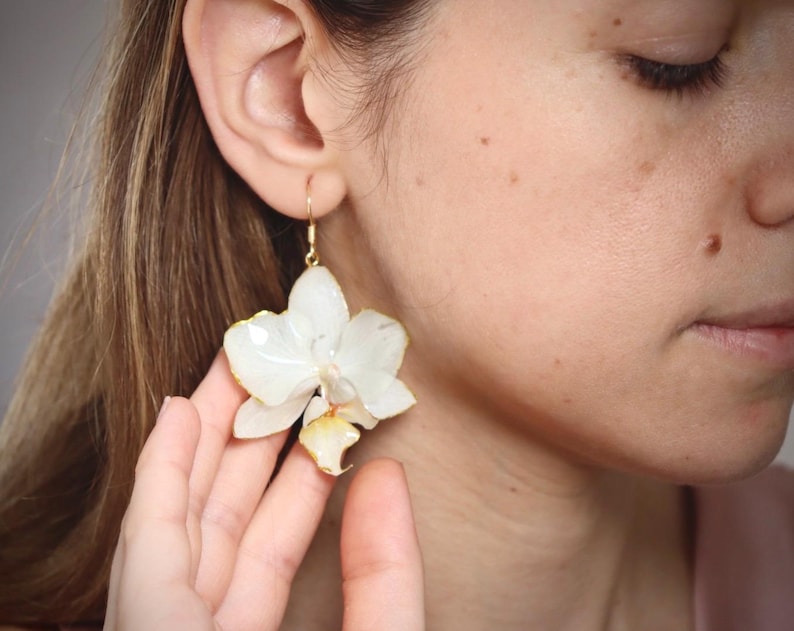 May include: White orchid flower earrings with gold-tone hooks. The earrings are made with real pressed flowers.