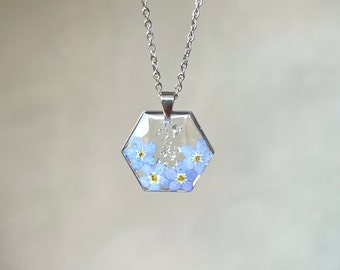 Collier en résine avec myosotis et feuilles dorées ou argentées. Pendentif hexagonal en résine avec de véritables fleurs de myosotis.