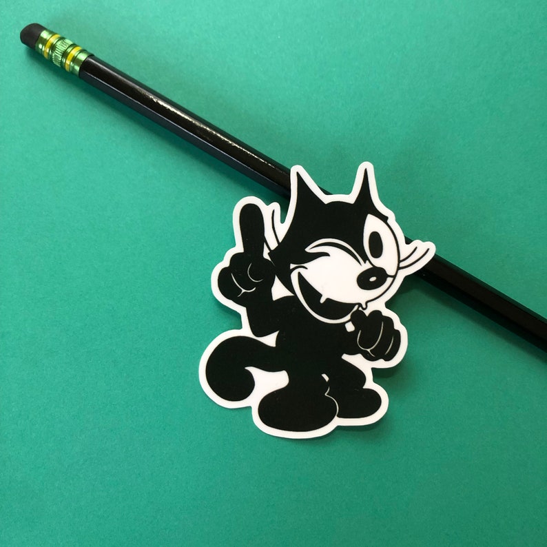 Puede incluir: Pegatina de dibujos animados en blanco y negro de un gato con un ojo gui&ntilde;ando y una pata levantada. El gato lleva una sonrisa traviesa.