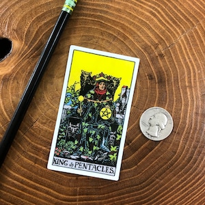 May include: King of Pentacles tarot card featuring a man sitting on a throne with a pentagram in his hand. The card is yellow with black outlines and the text "KING of PENTACLES" at the bottom.
