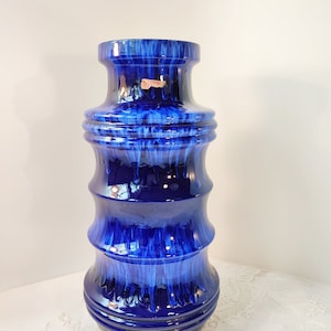 May include: A tall, blue ceramic vase with a textured, drip-like glaze. The vase has a wide base and a narrow neck.