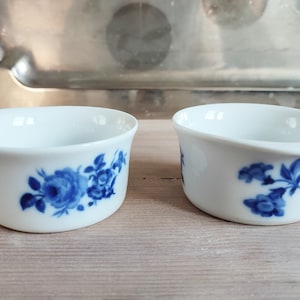 Puede incluir: Dos cuencos de cerámica blanca con diseños florales azules. Los cuencos son redondos y tienen un ligero borde alrededor del borde. Los diseños florales son diferentes en cada cuenco.