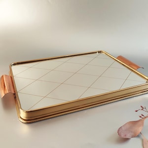 May include: A gold-colored serving tray with a mirrored surface and a diamond pattern. The tray has two copper-colored handles.