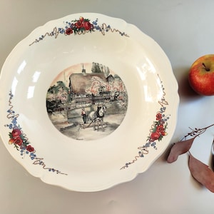 Puede incluir: Un plato de servir de cerámica blanca con un borde festoneado. El plato presenta una escena pintada de una cabaña con un carruaje tirado por un caballo y un borde floral.