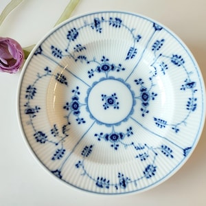May include: A white ceramic plate with a blue floral pattern. The plate has a fluted edge and a central design with a circle in the middle.