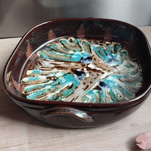 Może przedstawiać: Brązowa ceramiczna forma do pieczenia z abstrakcyjnym wzorem w kolorze turkusowym, białym i brązowym. Forma ma dwa uchwyty po bokach.