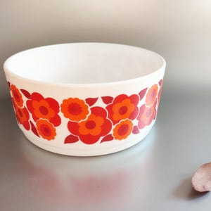 Könnte beinhalten: Weiße Keramikschüssel mit rotem und orangefarbenem Blumenmuster. Die Schüssel ist rund und hat einen breiten Rand.