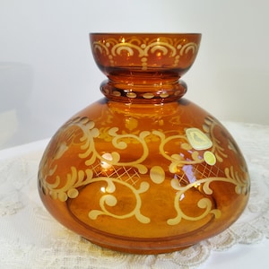 May include: Amber glass vase with a white etched floral design. The vase has a wide base and a narrow neck.