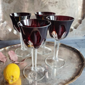 Könnte beinhalten: Vier klare Weingläser aus Glas mit einer dunkelroten, fast schwarzen Tönung. Die Gläser stehen auf einem silbernen Tablett mit einer Zitrone daneben.