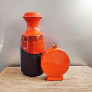 May include: Two ceramic vases in orange and black. The larger vase is tall and narrow with a rounded base. The smaller vase is round and has a flat base.