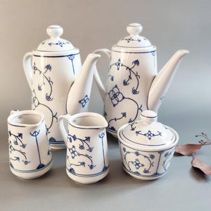 Puede incluir: Un juego de té de porcelana blanca con diseños florales azules. El juego incluye dos teteras, dos jarras pequeñas y un azucarero con tapa. El patrón azul presenta flores y vides.