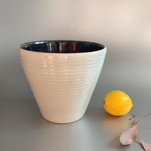 May include: White ceramic planter with a dark blue and green glaze on the inside. The planter has a ribbed design and is shaped like a cone.