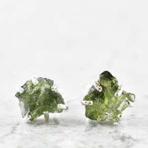 Op de afbeelding: Een paar zilveren oorbellen met groene edelsteen accenten. De edelstenen zijn ruw en onregelmatig van vorm, waardoor de oorbellen een natuurlijke en organische uitstraling krijgen.