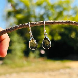 May include: A pair of silver dangle earrings with teardrop-shaped green gemstones.