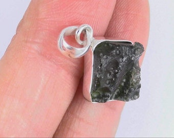 May include: A silver pendant featuring a dark green, rough, and irregularly shaped stone.
