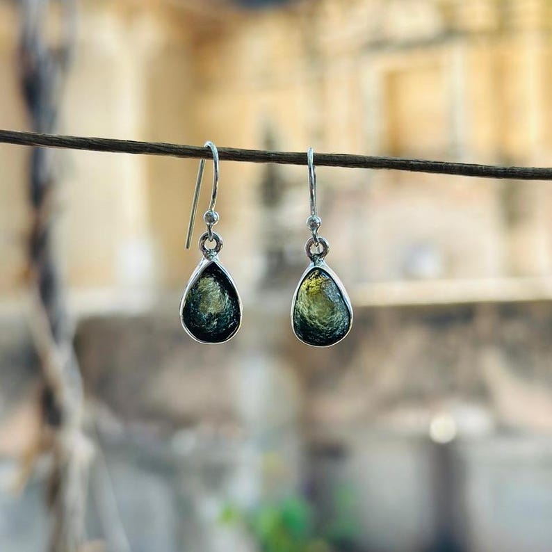 May include: A pair of silver dangle earrings with teardrop-shaped green and gold gemstones.
