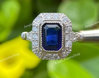 May include: A silver ring with a large, dark blue, emerald-cut gemstone surrounded by smaller, clear gemstones.