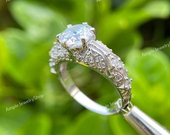 May include: A silver engagement ring with a large, clear, round-cut center stone and smaller stones set in a delicate, floral design.