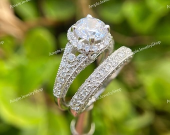 May include: A silver engagement ring set with a large round center stone surrounded by smaller stones. The band is decorated with a delicate floral pattern.