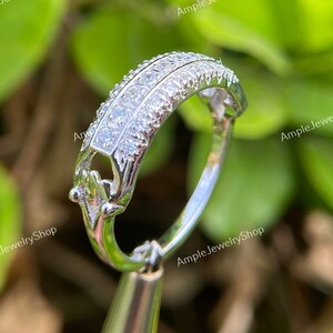 May include: A silver ring with a delicate design featuring a row of small, clear stones. The ring is set on a silver stand.