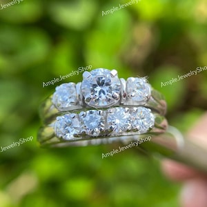 May include: A silver wedding band set with three round diamonds on each band. The center diamond on the top band is larger than the other diamonds.