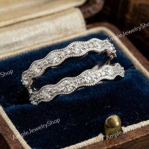 May include: A silver-toned ring guard featuring two wavy bands connected at the base. Each band is set with a series of small, clear, round-cut stones and finished with a delicate milgrain edge detail along the top and bottom of the metal.