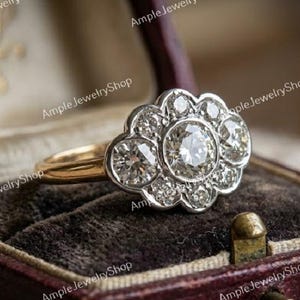 Może przedstawiać: Pierścionek w stylu vintage z kwiatowym wzorem z diamentów. Pierścionek ma złoty pierścień i srebrną oprawę dla diamentów. Leży w bordowym pudełku na biżuterię z aksamitnym wnętrzem.