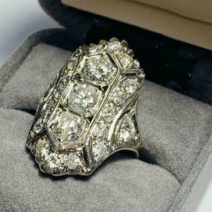 May include: A vintage-style diamond ring with a large, octagonal-shaped center stone surrounded by smaller diamonds. The ring is set in a white metal band and has a geometric design.