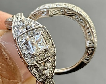 May include: A silver engagement ring set with a square-cut diamond surrounded by smaller diamonds. The band is decorated with intricate floral designs.