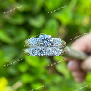 May include: A set of two silver rings with clear round diamonds. The larger ring has a single larger diamond in the center and two smaller diamonds on either side. The smaller ring has five smaller diamonds set in a row.