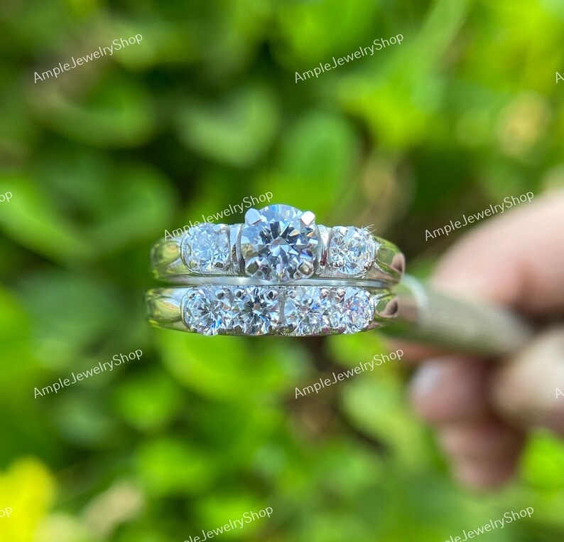 May include: A set of two silver rings with clear round diamonds. The larger ring has a single larger diamond in the center and two smaller diamonds on either side. The smaller ring has five smaller diamonds set in a row.