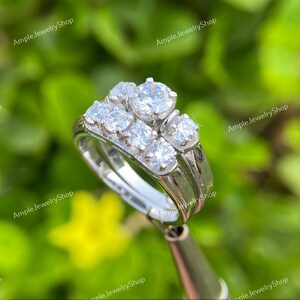 May include: A silver wedding band set with a cluster of five round-cut diamonds. The center diamond is larger than the surrounding diamonds.